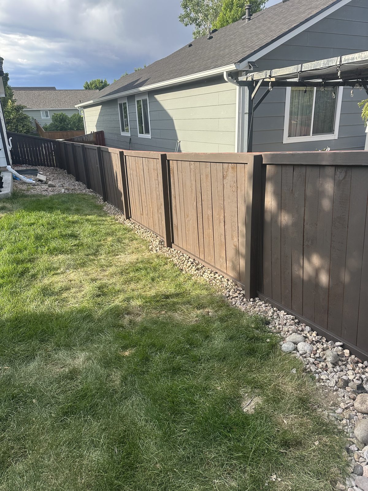Dark stained privacy fence with a river rock drainage border along the base