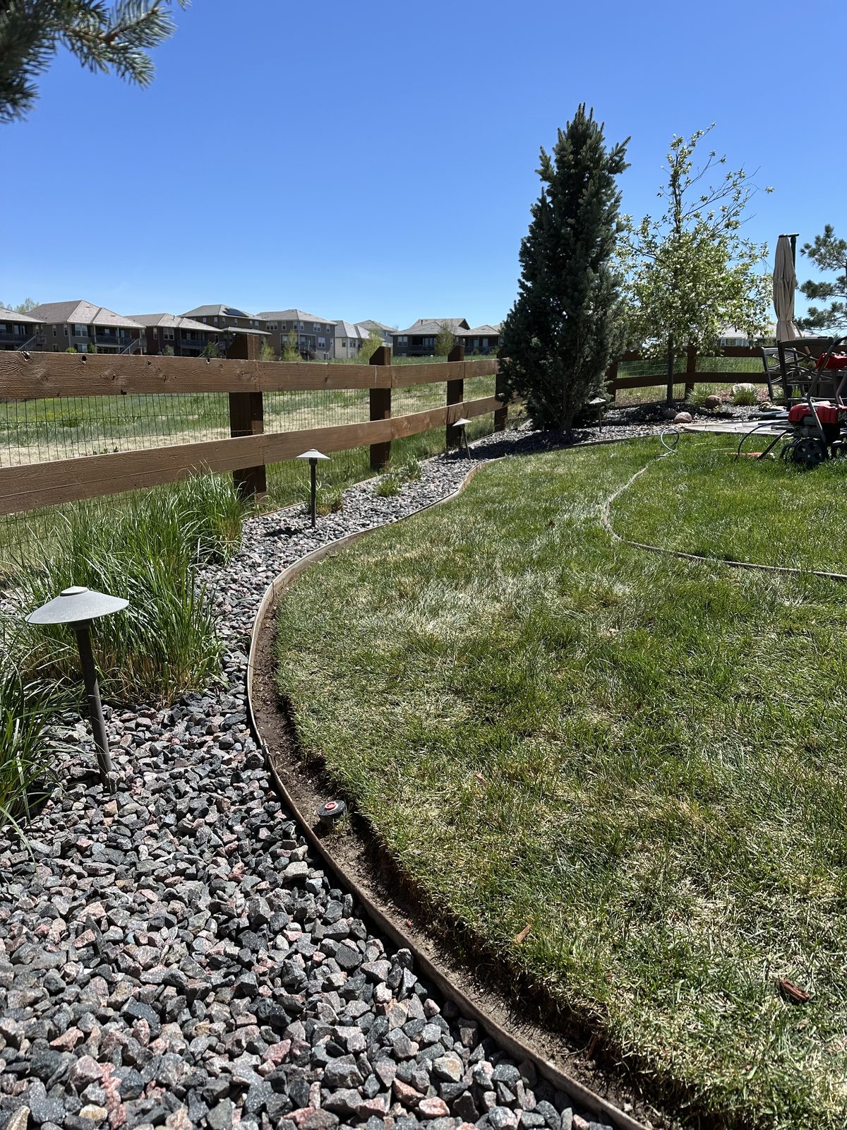 Curved steel edging separating lawn from a rock bed with path lighting